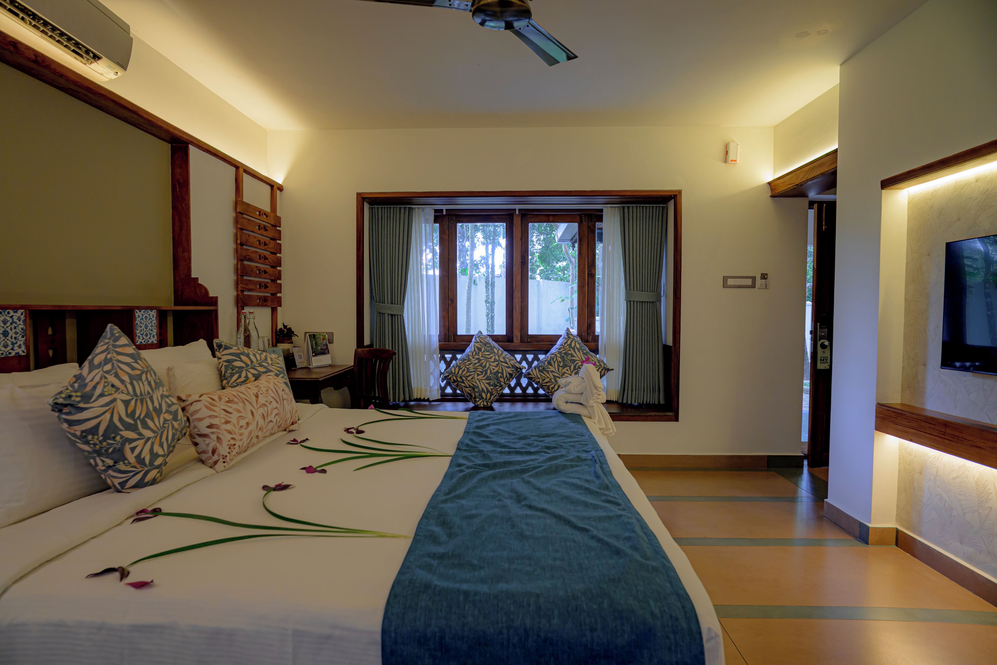 A hotel room with a large bed, a TV mounted on the wall, and a window with curtains.