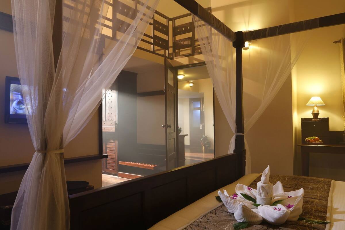 Un dormitorio con cama con dosel, un espejo grande y vista a una escalera.