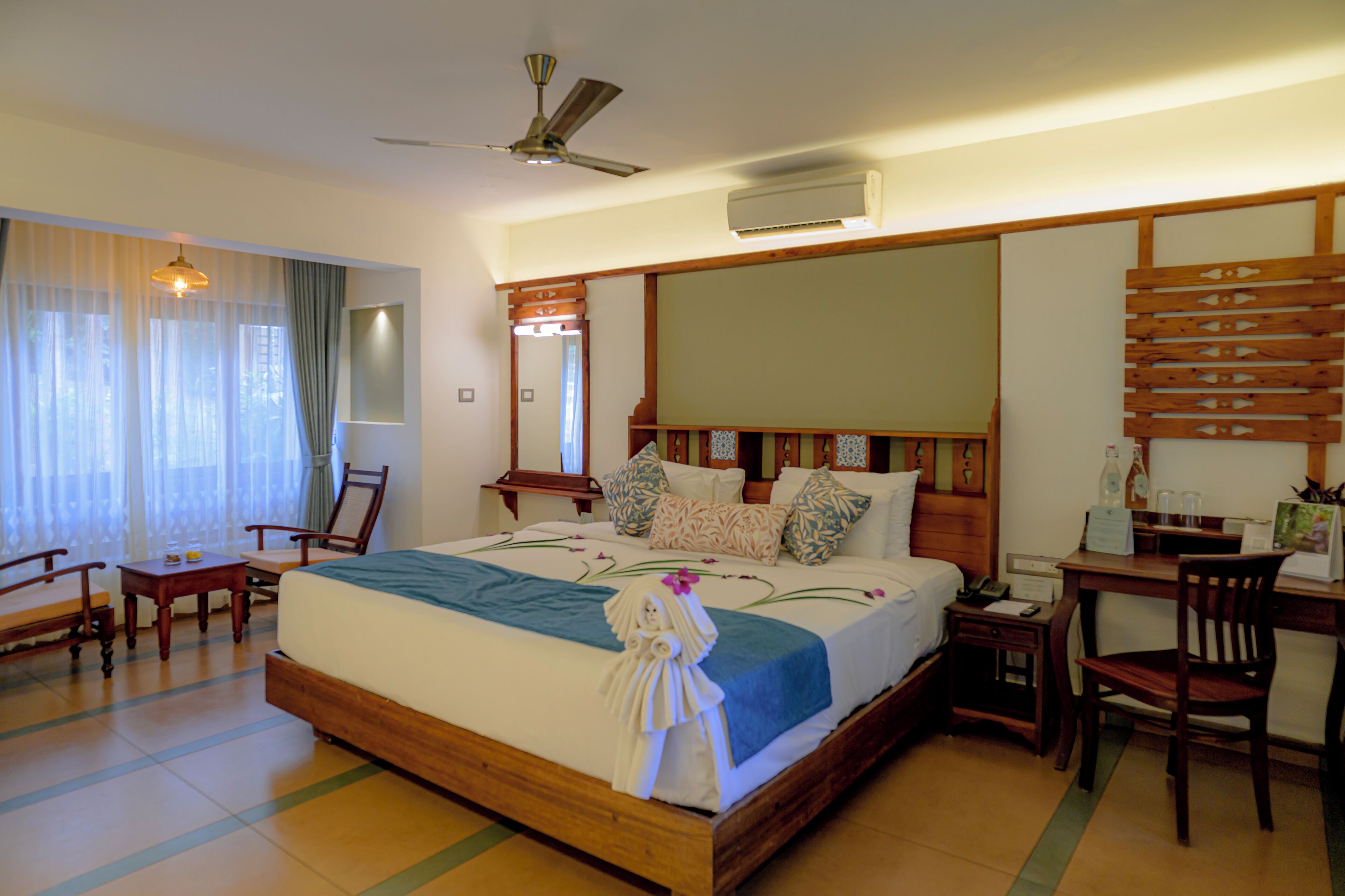 Habitación de hotel con cama, escritorio, silla, ventilador de techo y unidad de aire acondicionado.