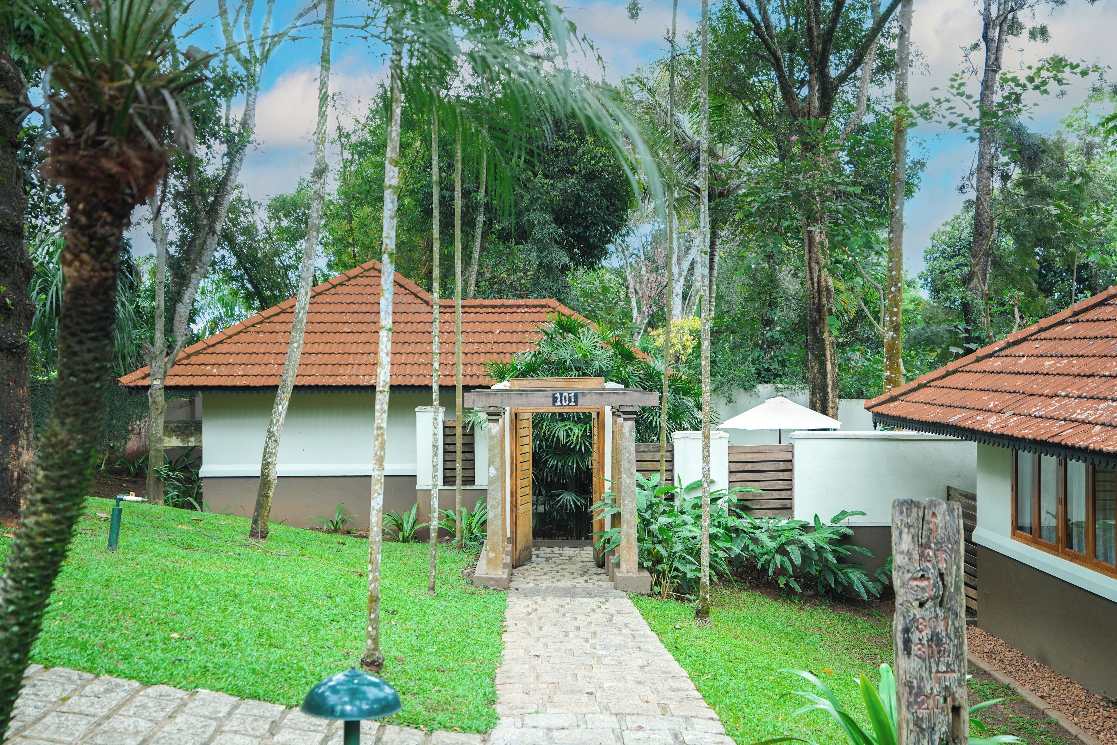 A pathway leading to a building with a tiled roof, surrounded by lush greenery and trees.