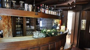 A bar area with wooden bar stools, shelves with bottles and glasses, and a brick floor. - Landhotel Binderhausl (Inzell)