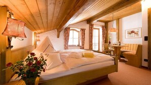 A cozy bedroom with a wooden ceiling, a bed with white linens, a bedside table with a lamp, and a vase of red flowers. - Landhotel Binderhausl (Inzell)