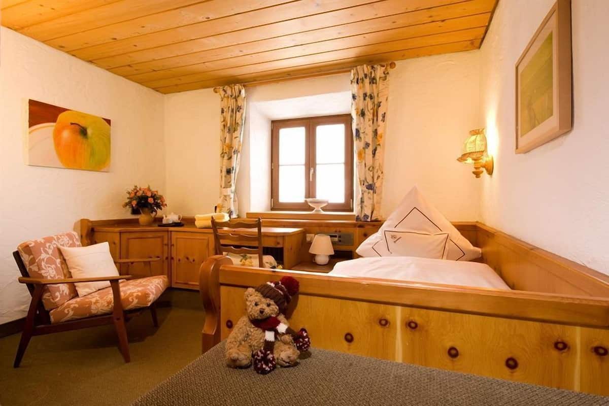 A cozy room with a wooden bed, a chair, a small table, and a teddy bear.