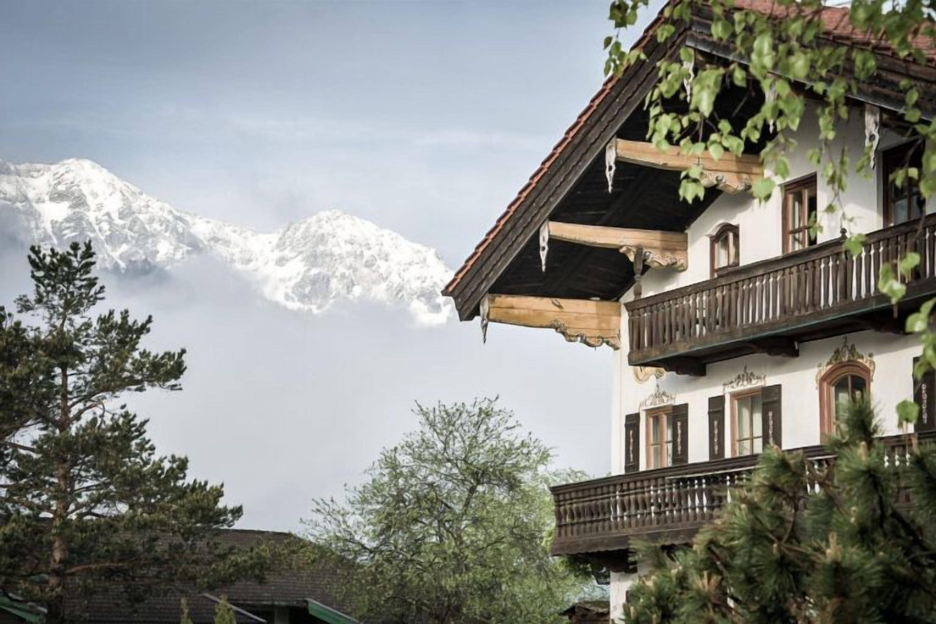 Un chalet traditionnel doté d’un balcon, entouré d’arbres et avec des montagnes en toile de fond.