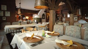 A restaurant with wooden beams, tables set with white tablecloths, and hanging copper light fixtures. - Landhotel Binderhausl (Inzell)