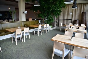 Ein Restaurant mit mehreren Tischen und Stühlen, einer grünen gepolsterten Bank und hängenden Pflanzen.