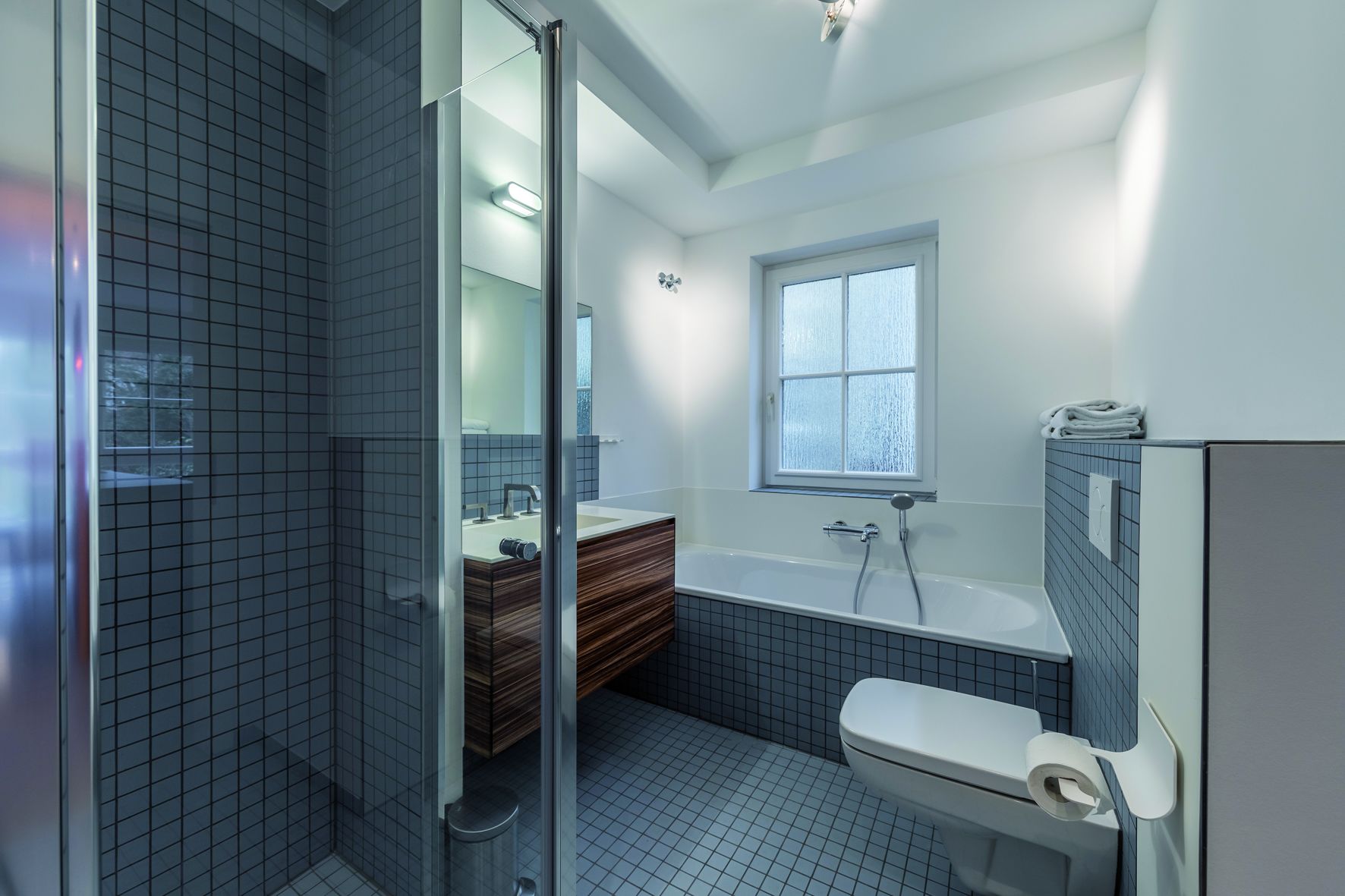 Un baño moderno con cabina de ducha de vidrio, una bañera independiente, inodoro y lavamanos con tocador de madera.