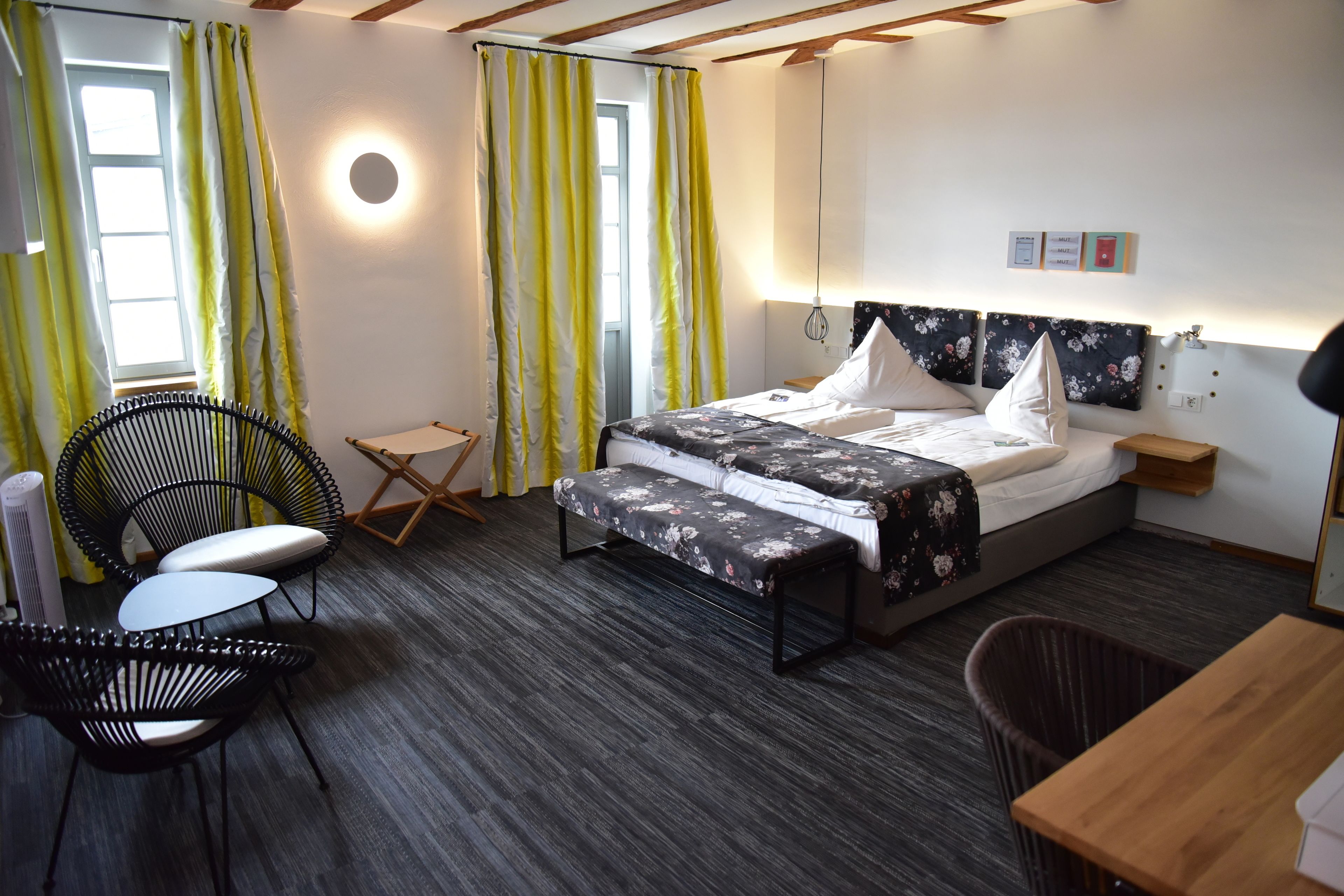 A bedroom with a bed, bedside tables, a desk, chairs, a radiator, and curtains.