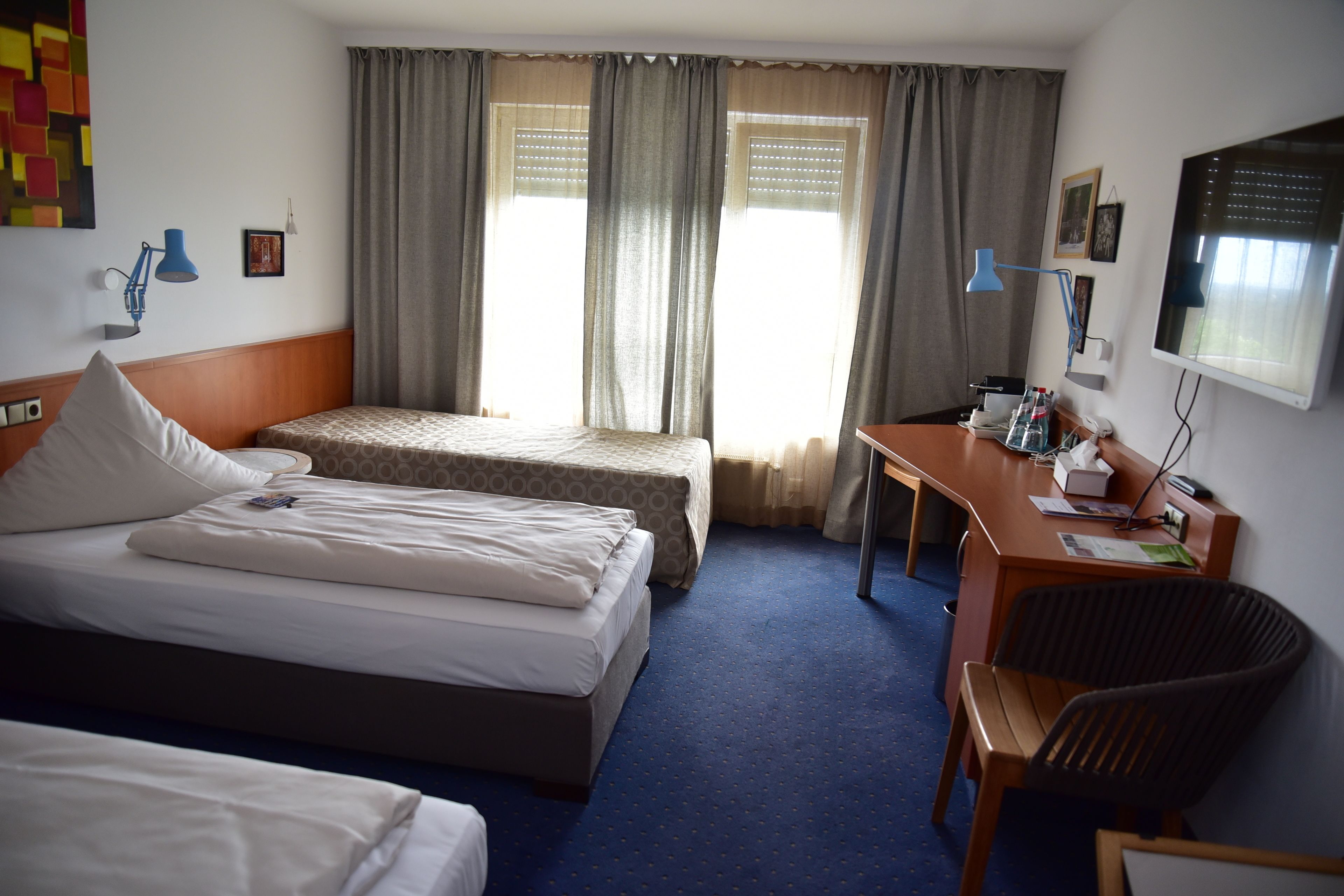 A hotel room with two beds, a desk, a chair, a TV, and a window with curtains.
