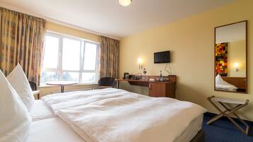 A hotel room with a large bed, a desk, a chair, a small table, a television, and a window with curtains.