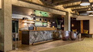 Un espace bar avec un comptoir en bois, des étagères remplies de verres et de bouteilles, et de grands récipients en métal.