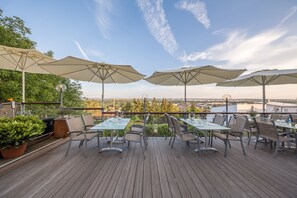 Eine Terrassengaststätte mit Tischen, Stühlen, großen Sonnenschirmen und Pflanzen in Töpfen.