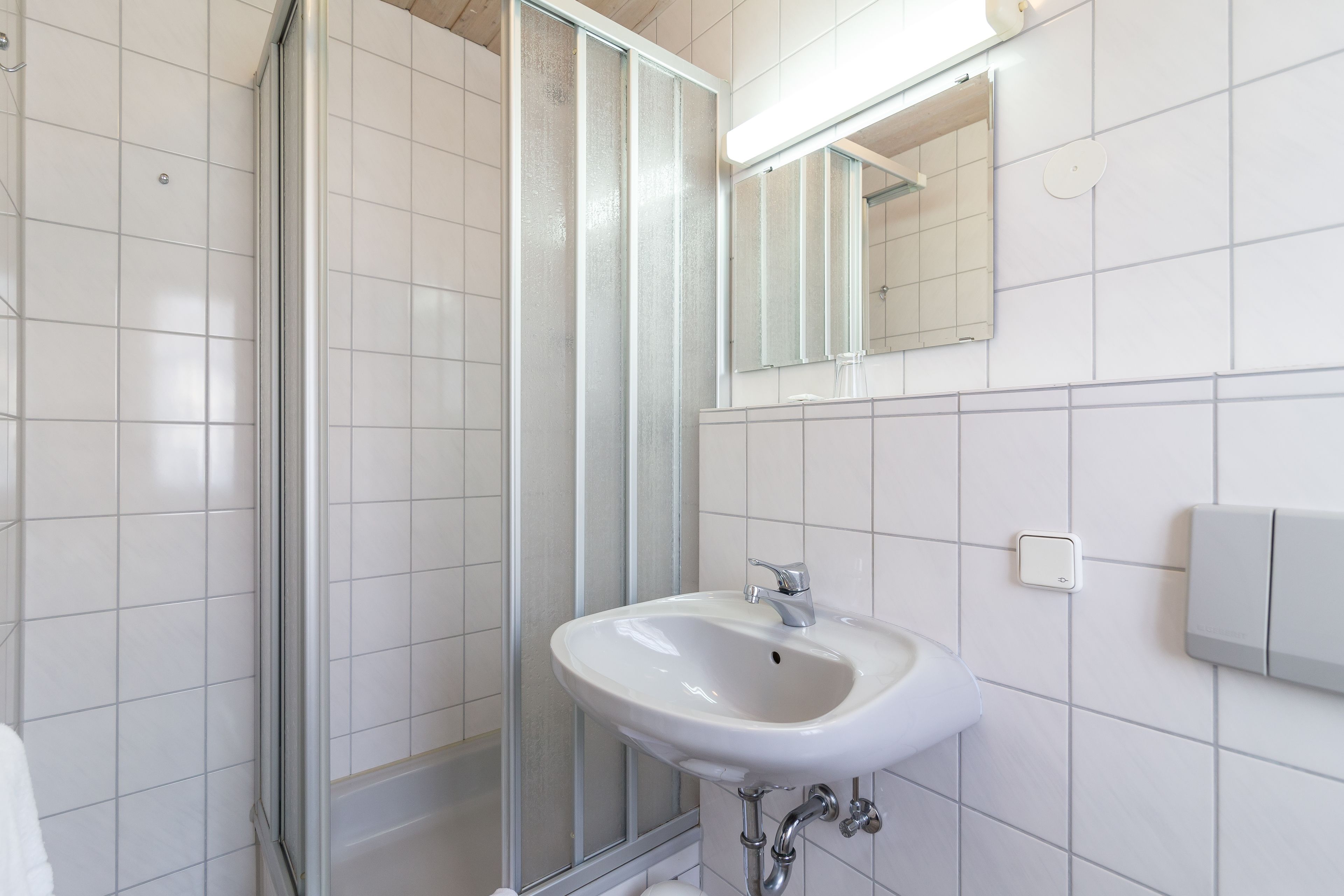 Une salle de bain avec un lavabo blanc, une cabine de douche en verre et un miroir au-dessus du lavabo.