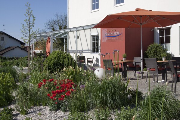 A restaurant patio with outdoor seating, a garden with red tulips, and a sign for 'INITALHOF'.