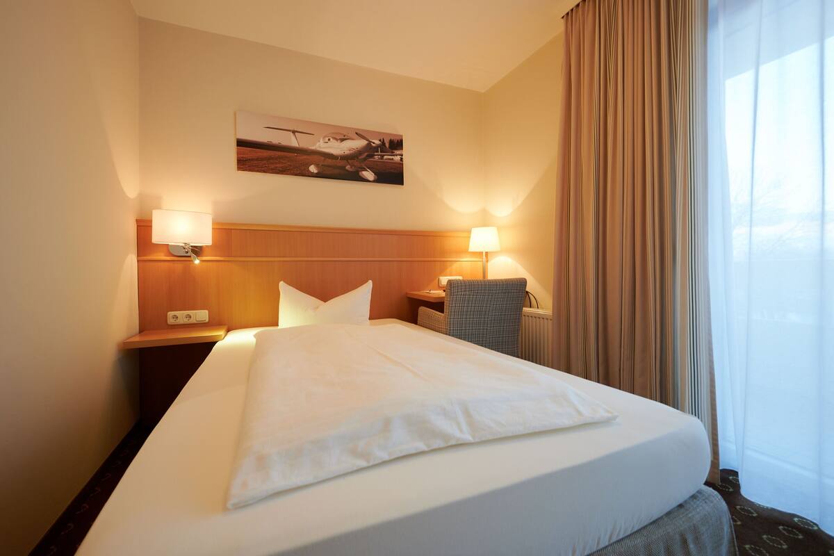 Une chambre d’hôtel avec un grand lit, deux lampes de chevet, une tête de lit, un bureau, une chaise et une fenêtre avec des rideaux.
