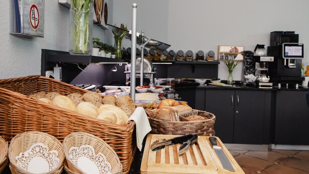 A kitchen area with a variety of breads and pastries, a coffee machine, and a cutting board with a knife. - Friends Hotel Kerpen (Kerpen)