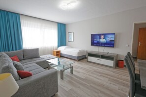 A modern living room with a sofa, a glass coffee table, a bed, a TV, and a wooden floor. - Friends Hotel Kerpen (Kerpen)