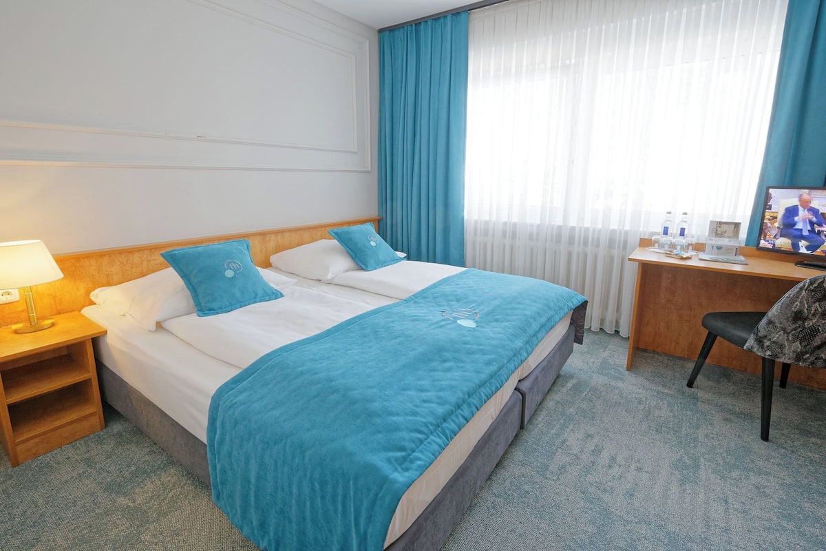 A hotel room with a bed, a desk, a chair, and a TV.