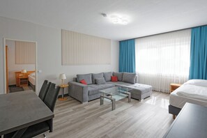 A modern hotel room with a grey sofa, a glass coffee table, a wooden side table, and a bed with white bedding. - Friends Hotel Kerpen (Kerpen)