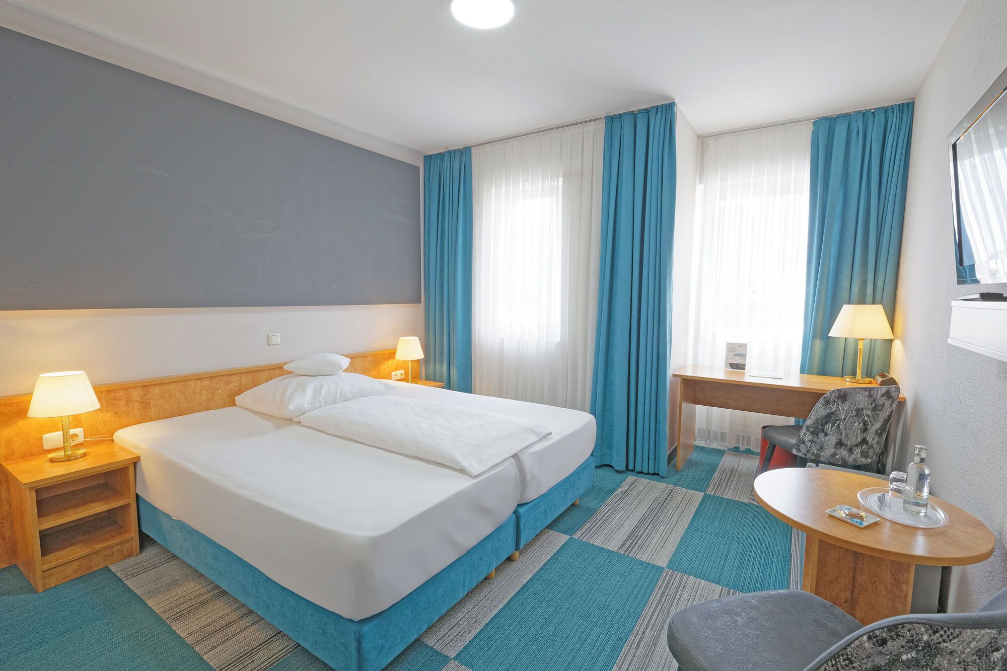 Une chambre d’hôtel avec un lit double, un bureau, une chaise, une petite table et une fenêtre avec des rideaux.