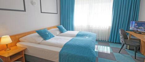 A hotel room with a bed, a desk, a chair, a TV, and a window with curtains.