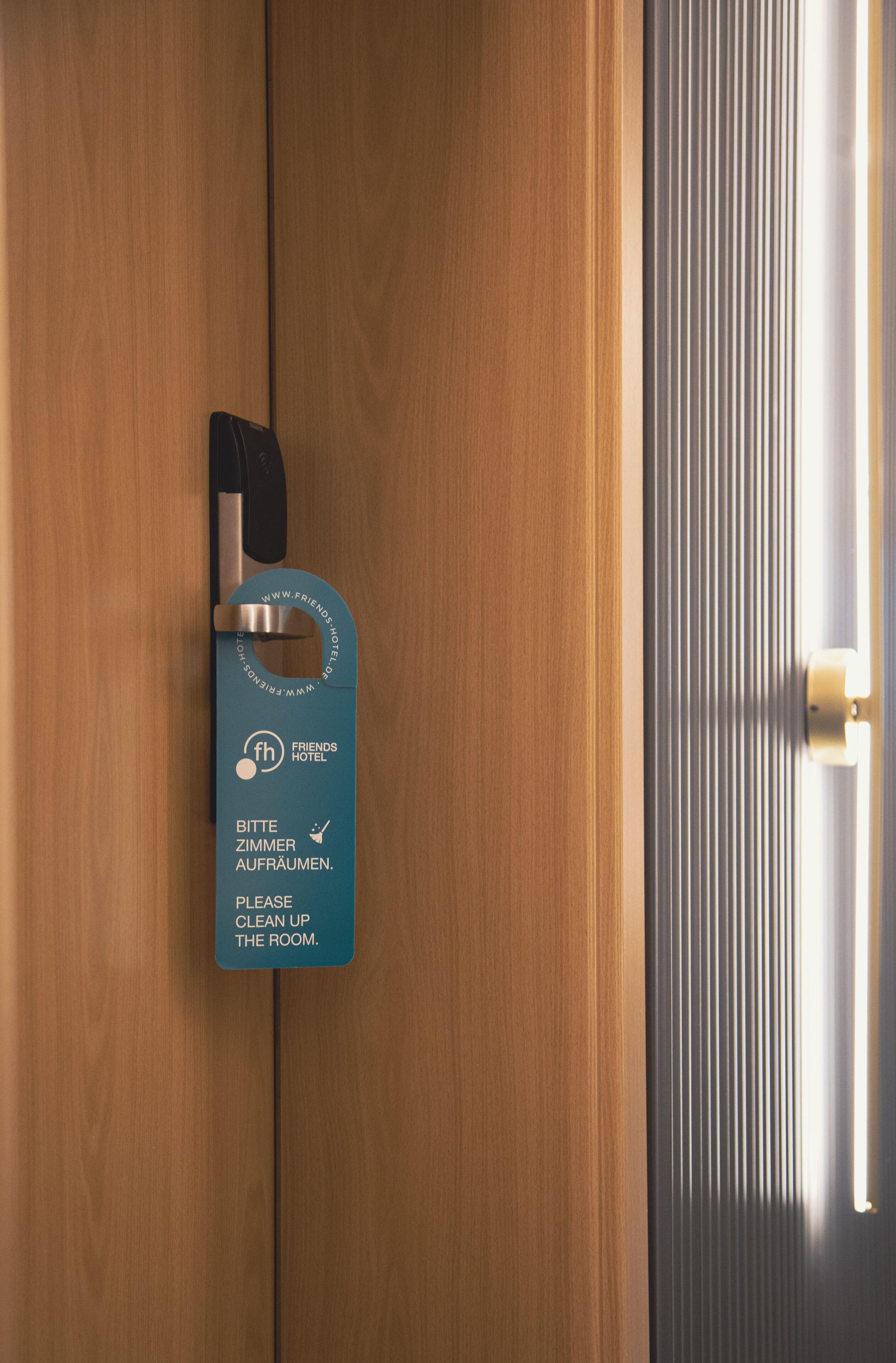 Una puerta de madera con un picaporte de metal y un letrero azul que dice 'Por favor, ordenen la habitación'.
