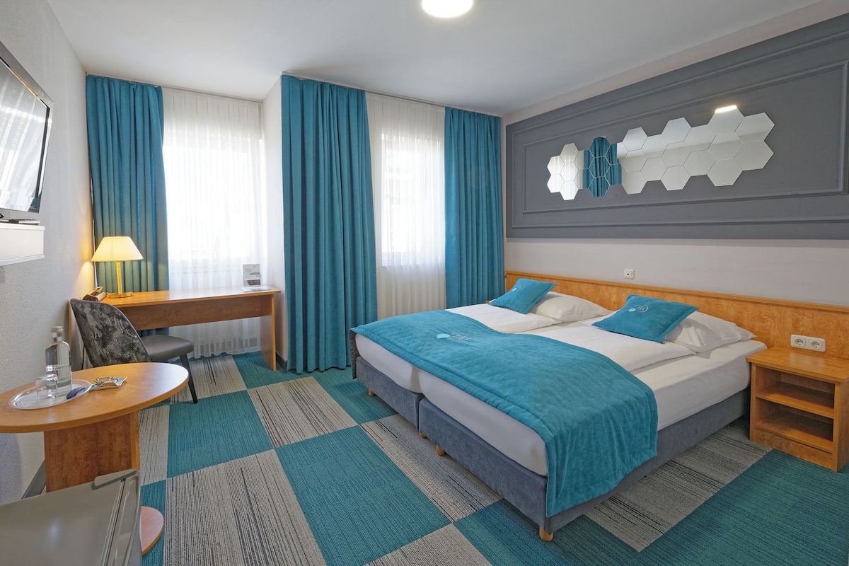 A hotel room with a bed, desk, chair, and a wall-mounted TV.
