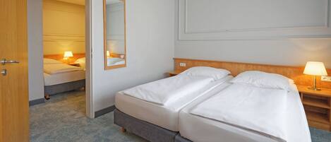 Une chambre d’hôtel avec un lit double, une table de chevet avec une lampe, un miroir et une porte donnant sur une autre pièce.