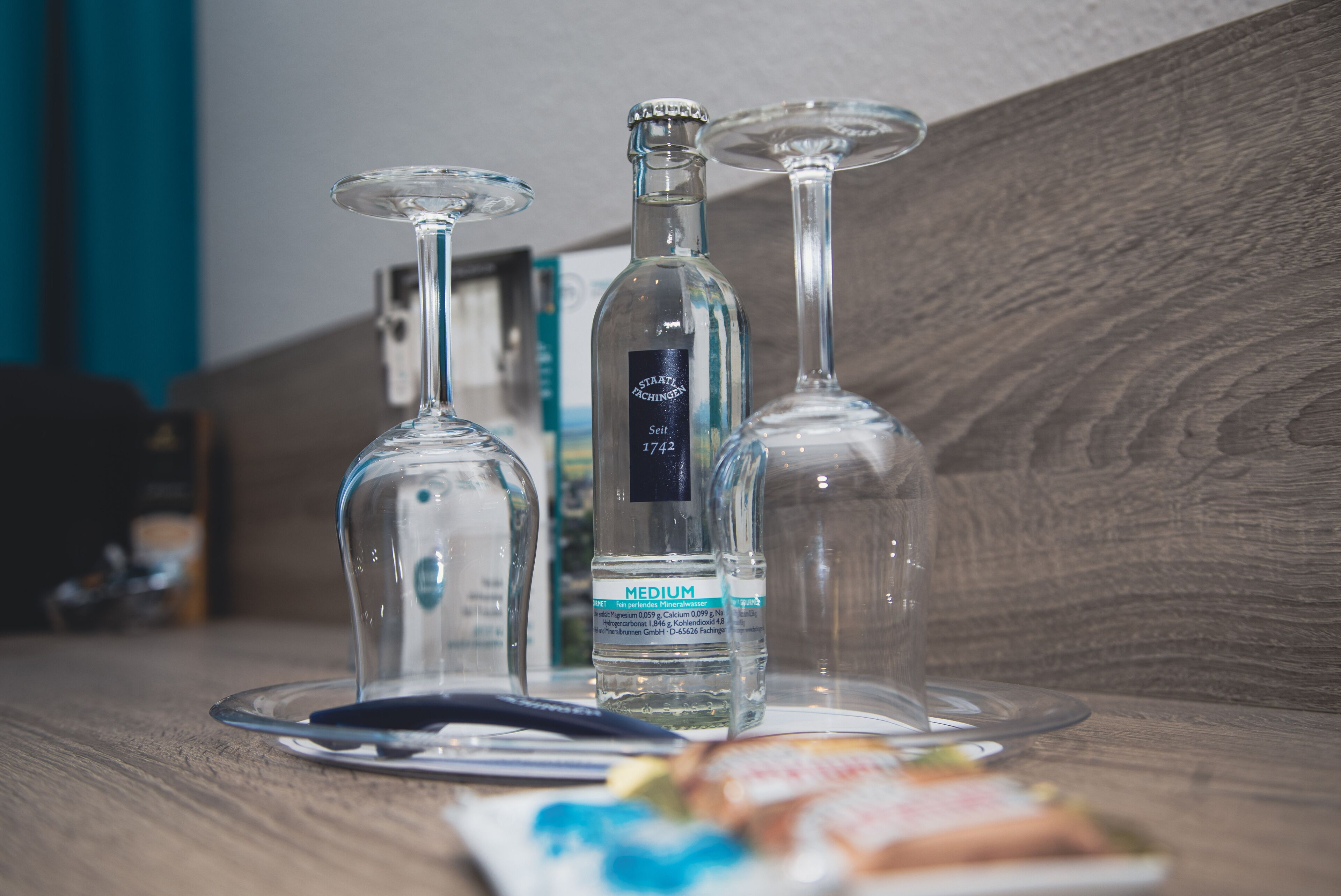 A table with three clear glass bottles and two wine glasses on a wooden surface.