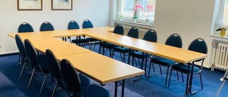 Un salón de conferencias con una mesa larga, sillas, obras de arte enmarcadas en la pared y una ventana con plantas.