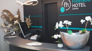 A reception desk with a computer, a phone, and a sign for 'Friends Hotel Kerpen'. - Friends Hotel Kerpen (Kerpen)
