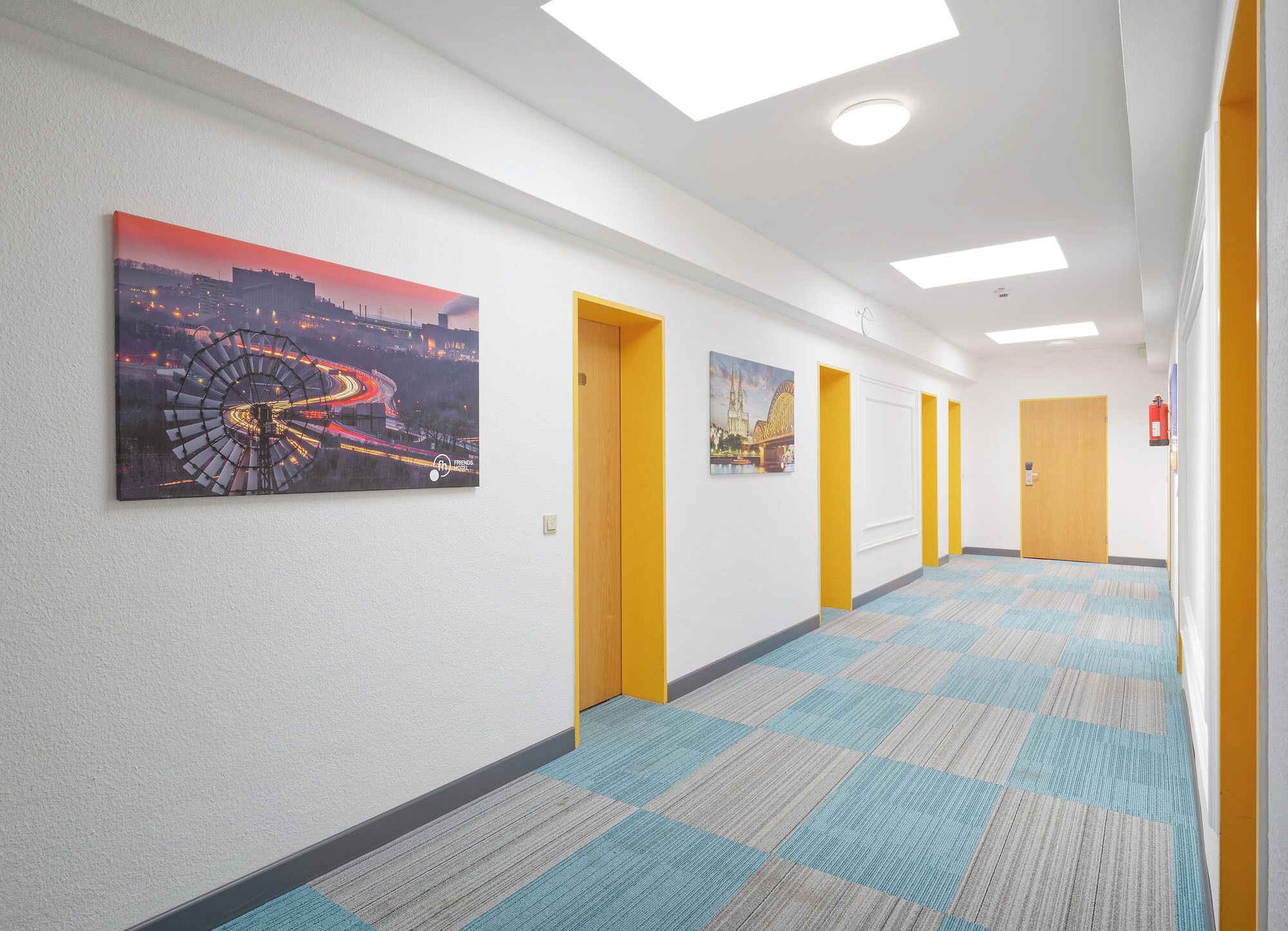A hallway with artwork on the walls, doors, and a patterned carpet.