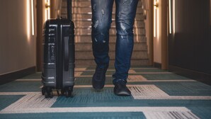A person with a suitcase in a hallway with patterned carpet and wall-mounted lights. - Friends Hotel Kerpen (Kerpen)