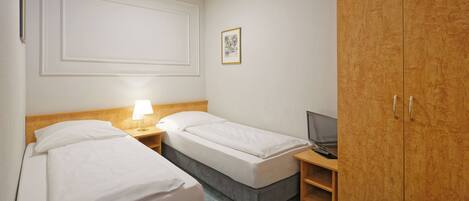 A hotel room with two beds, a wooden wardrobe, a desk with a lamp, and a framed picture on the wall.