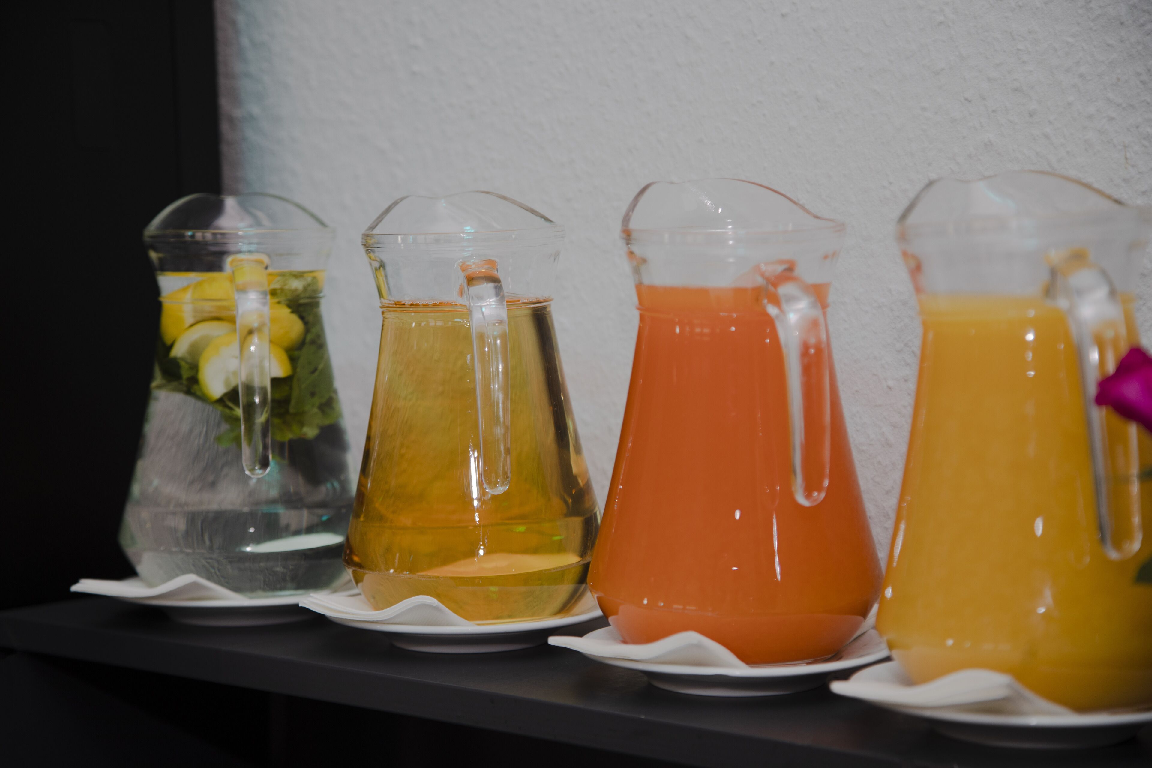 Four pitchers of beverages on a shelf.