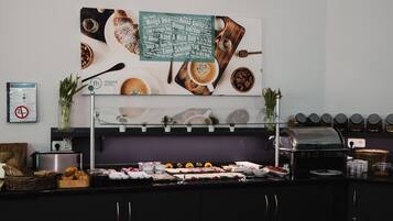 Ein reichhaltiges Frühstücksbuffet mit verschiedenen Speisen, einer Kaffeemaschine und einem Schild mit positiven Botschaften.