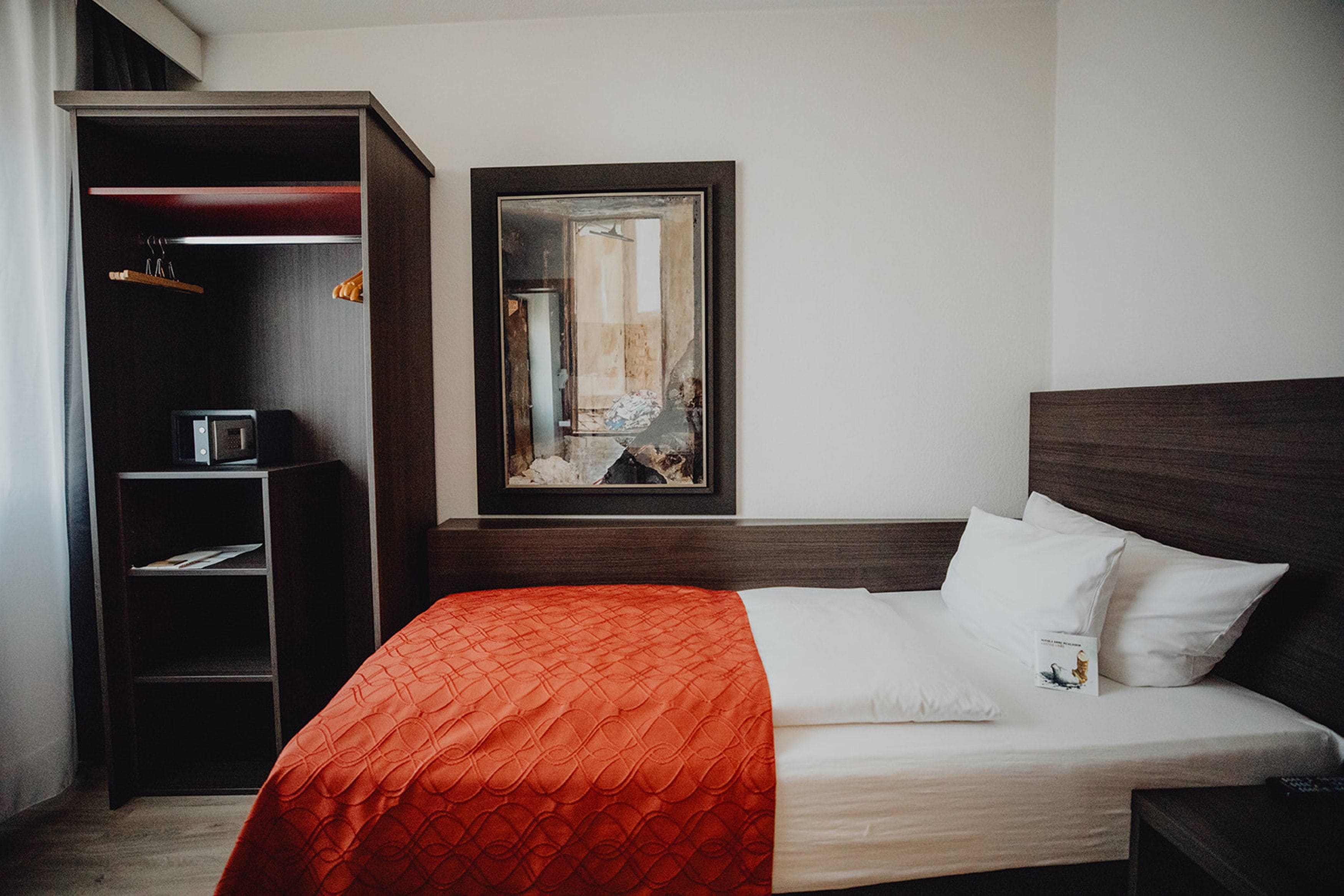 Una habitación de hotel con cama, armario y un cuadro en la pared.