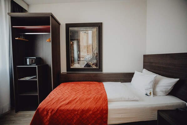 Una habitación de hotel con cama, armario y un cuadro en la pared.