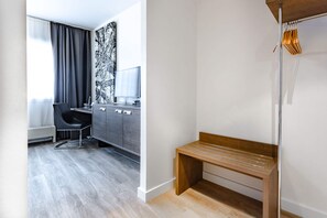 A modern hotel room with a grey wardrobe, a wooden bench, a desk with a chair, and a large window with curtains. - Art Business Hotel Nürnberg (Nuremberg)