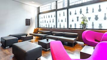 Un salón moderno con asientos negros y rosados, un ventanal con siluetas de jarrones y una pequeña planta sobre una mesa.