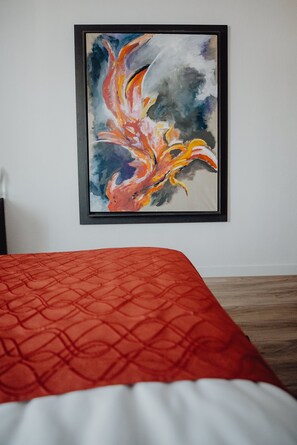 A bed with a red quilted cover, a framed abstract painting on the wall, and a wooden floor. - Art Business Hotel Nürnberg (Nuremberg)