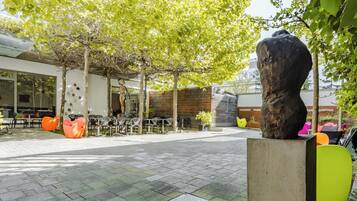 Un espacio al aire libre con sillas y mesas modernas, rodeado de árboles y una gran escultura.