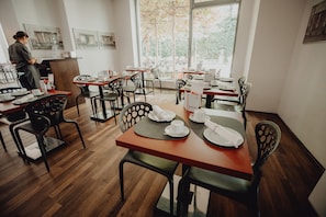 Un restaurante con pisos de madera, sillas negras y mesas dispuestas para comer.