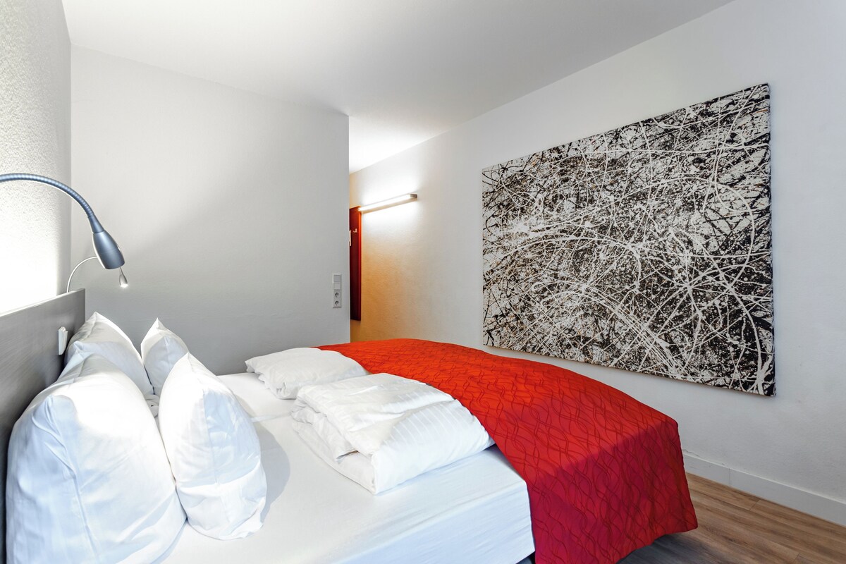 Una habitació d'hotel moderna amb un llit ben fet, un quadre abstracte gran a la paret i una làmpada de nit.