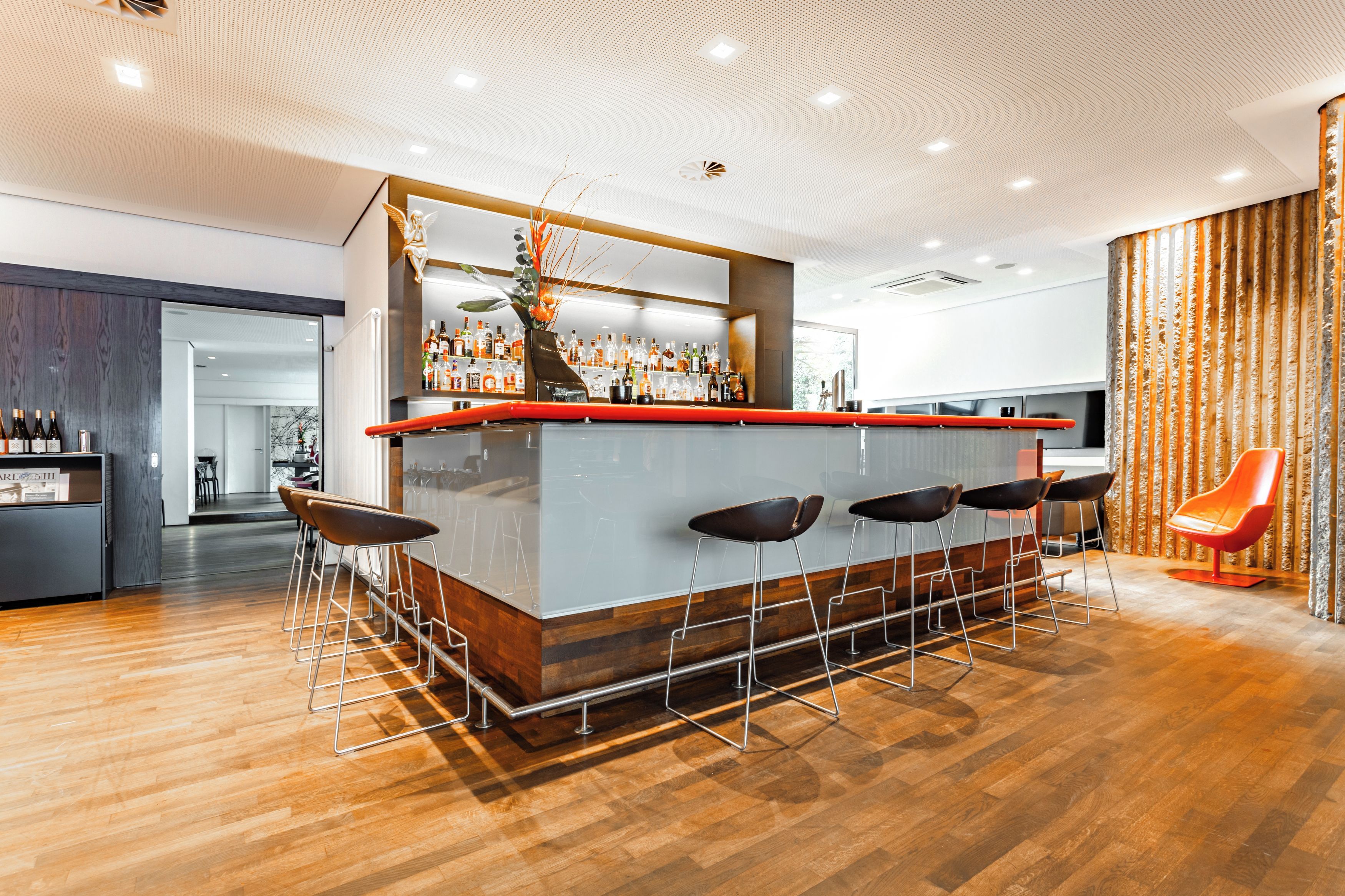 Uma área de bar moderna com balcão de madeira, vários bancos e uma planta decorativa.