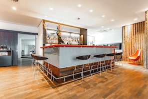 Un área de bar moderna con mostrador de madera, varios taburetes y una planta decorativa.
