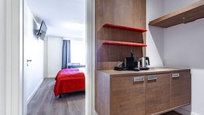 Habitació d'hotel moderna amb un armari de fusta, un llit amb mantell vermell i una televisió penjada a la paret.