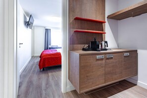 A modern hotel room with a wooden cabinet, a bed with a red cover, and a TV mounted on the wall. - Art Business Hotel Nürnberg (Nuremberg)