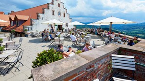 An outdoor patio with tables and chairs, a brick wall, and a building with a red roof in the background. - Hotel Ritter Durbach (Durbach)