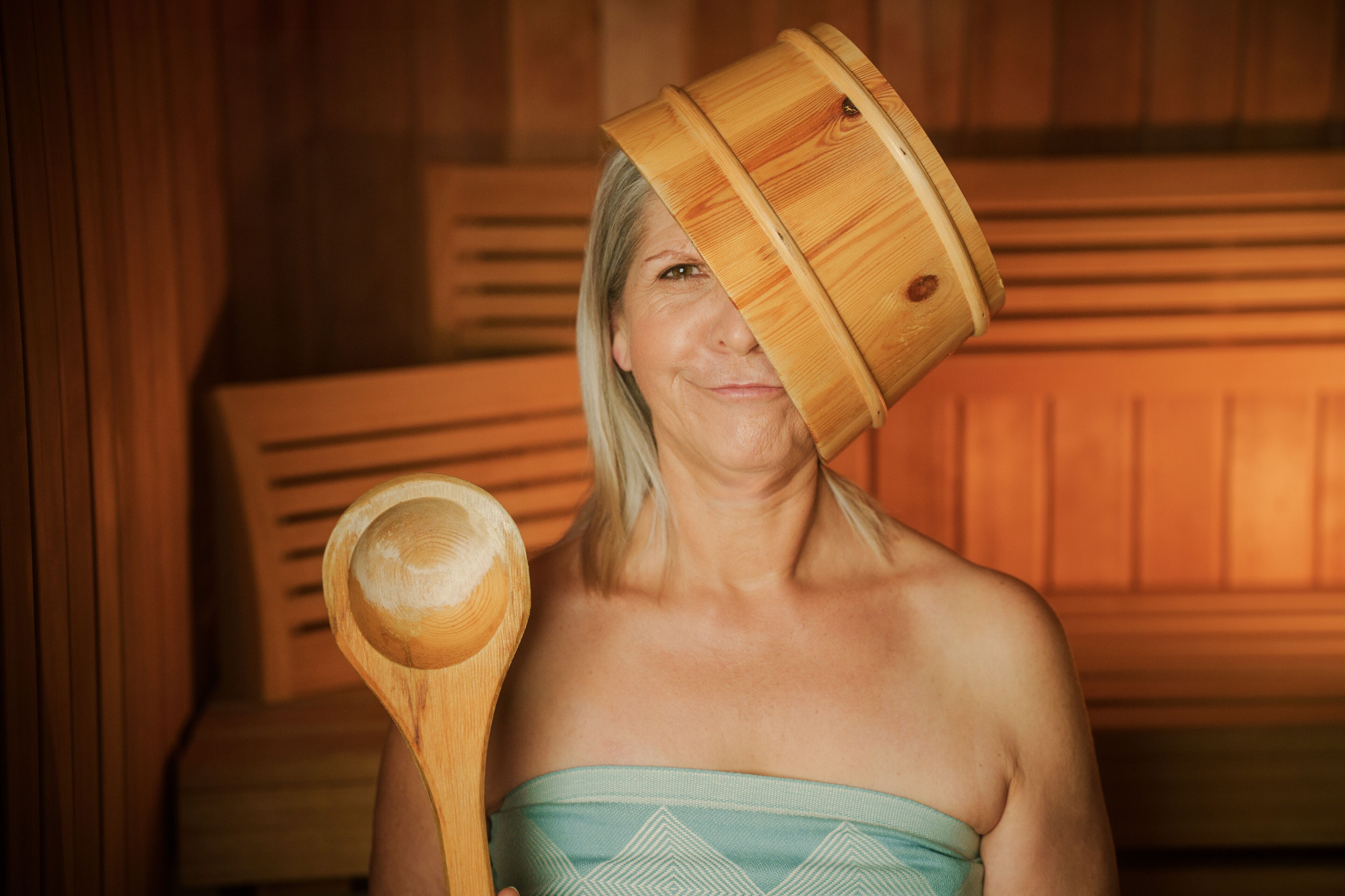 A person in a wooden cabin with a wooden bucket on their head and a wooden spoon in their hand.